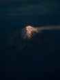 Dawn aerial photograph: first light touching only the snowy crown of a mountain, the valleys below still deep blue.