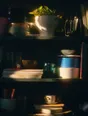 Prism-light photograph: A crowded shelf of mismatched things with hard sun combing across them.