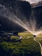 Motion photograph: a garden sprinkler running hard on cut grass at midday, the thrown water lit from behind and a bike dropped on the lawn