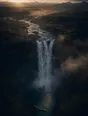 Dawn aerial photograph: an immense waterfall at first light with a tiny calm pool and stone step at its base.