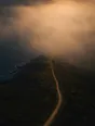 Dawn aerial photograph: a coastal path leading straight into luminous sea-fog glowing with hidden sun.