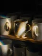 Prism-light photograph: One visibly uneven hand-thrown mug among identical machine-made ones on a shelf in hard sun.