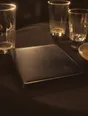 Struck-light photograph: the corner of a restaurant table after a meal, the bill folder set down, the glass rims catching light