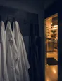 Dark cinematic photograph: A peg board of hanging jackets with one hook standing empty.