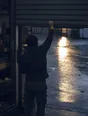 Dark cinematic photograph: A shutter going up on a shopfront at dawn with the light spilling out onto the wet street.