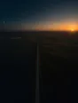 Dawn aerial photograph: a thin crescent moon low over dark plains opposite the sunrise, one straight farm track crossing between them.